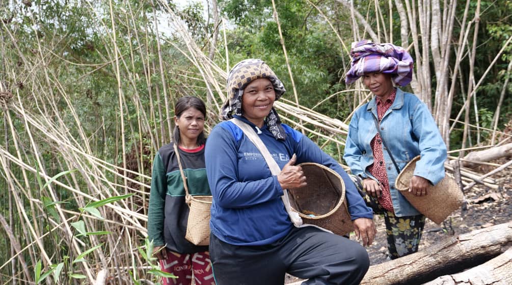 Three Dayak women with collecting baskets smile at the camera.