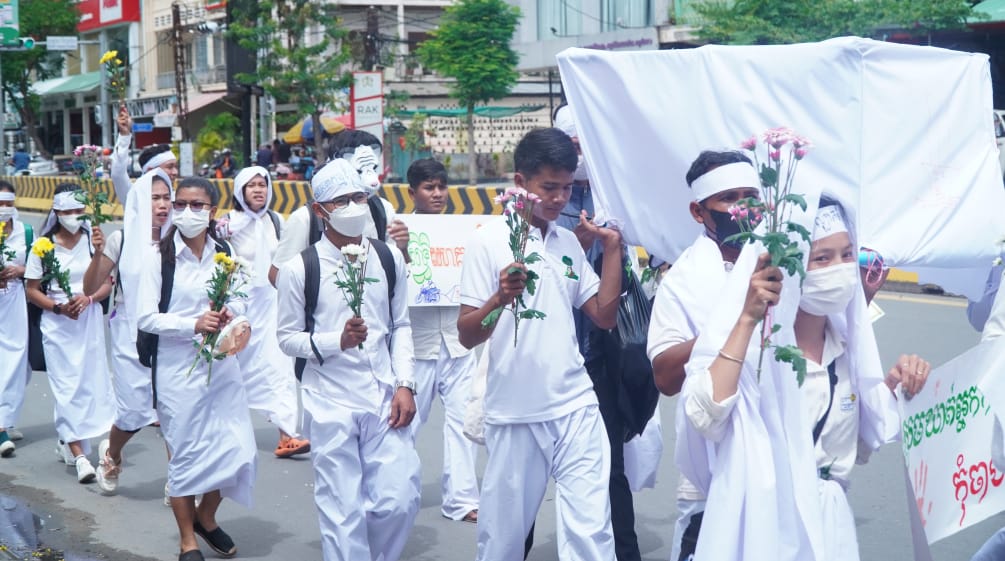 Young people dressed in white walk through a street in Phnom Penh with flowers in their hands