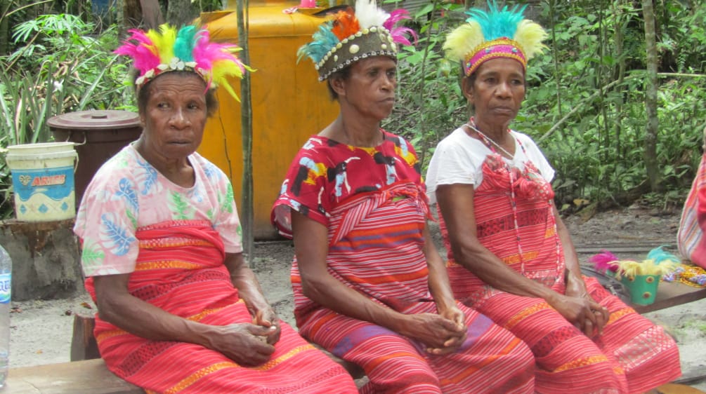 Three women dressed in red fabric and colorful feather headdresses