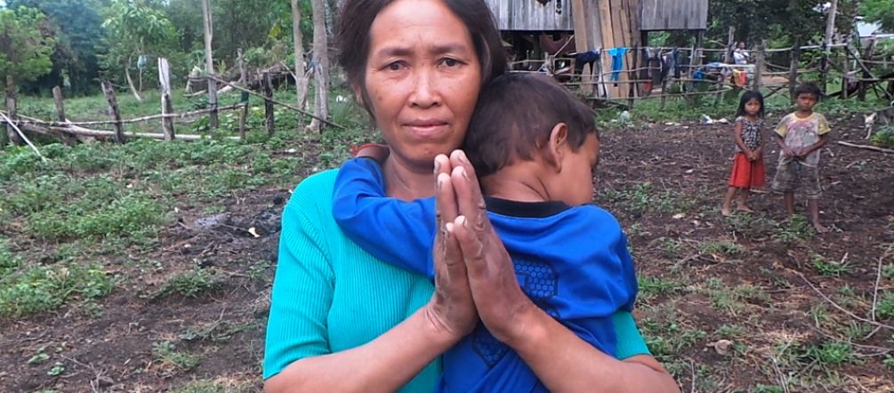 Driven off her land for sugar for the EU A woman holding a child, standing in front of their makeshift hut after being driven from their land