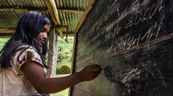 A young Ngäbe-Buglé woman writing on a blackboard