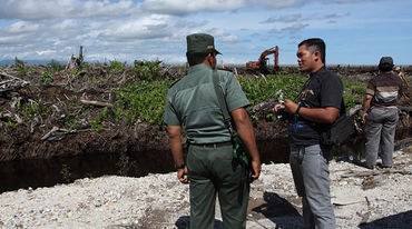 Two men standing infront of a clearance for palm oil palntation