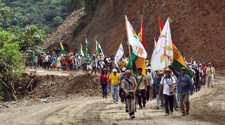 Indians on a protest march with flags in their hands walking up a gravel road