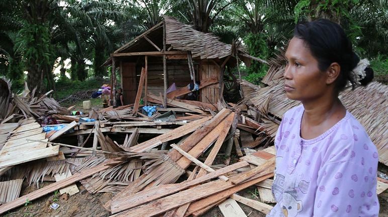 An indigenous woman stands in shock in front of her demolished house