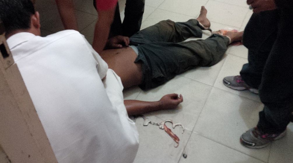 Fatal protest: a village chief beaten to death by plantation security thugs The corpse of a man lies on the floor. His head is not visible. Handcuffs are attached to one wrist and his feet are bound.