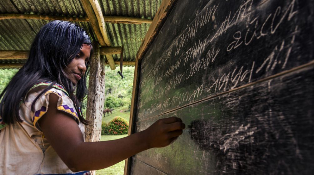A young Ngäbe-Buglé woman writing on a blackboard