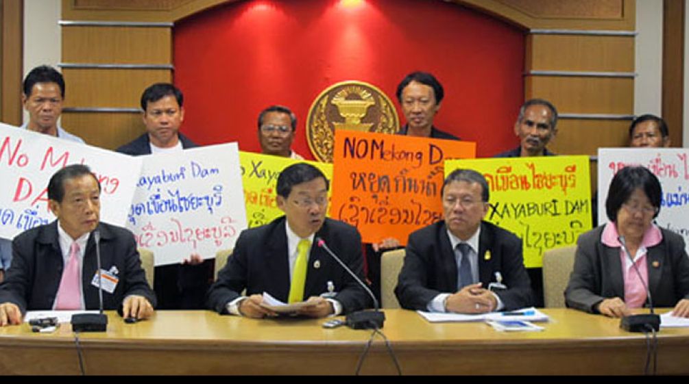 Politicians sitting at a table: Protesters behind them